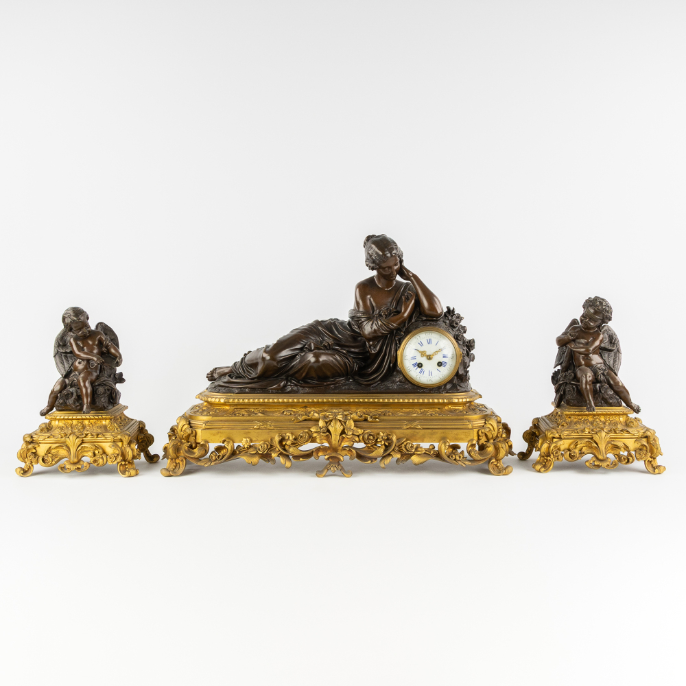 Henry Picard (XIX) een driedelige schouwgarnituur, klok en zijstukken, liggende dame en engelen, gepatineerd en verguld brons. (L:70 x W:21 x H:34 cm)